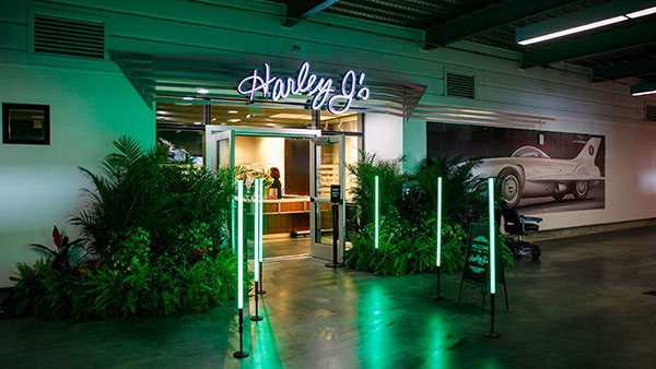 Entrance to Harley J's lounge at Daytona International Speedway with neon signage, green LED lights, and race-themed decor.