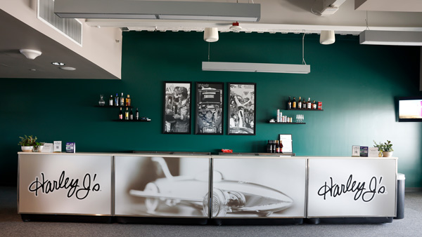 Harley J’s bar featuring a silver counter with vintage racing imagery, beverage displays and a dark green accent wall.